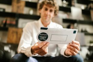 A man sitting indoors, reading an envelope with a cash back offer, blurred background.